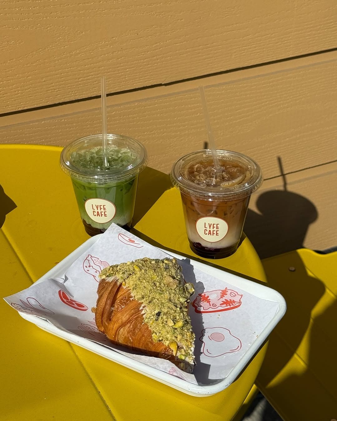 Matcha and iced coffee with pistachio croissant on yellow table